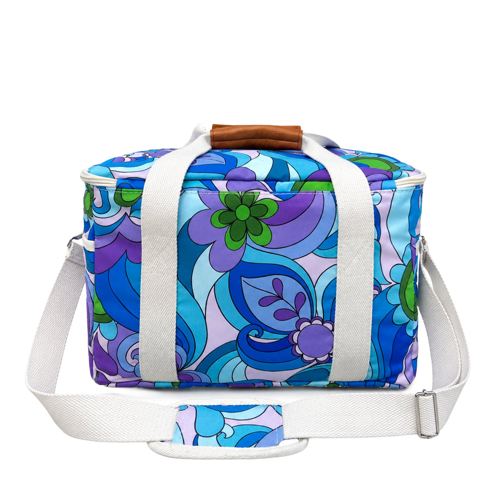 A rectangular duffel bag with a retro 1970s floral pattern in shades of blue, purple, and green, featuring white webbing handles and a brown leather top handle, shown on a plain white background.
