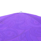 A close-up of a purple patio umbrella canopy with a subtle tonal swirl pattern, showing the fabric texture and the top finial against a white background.