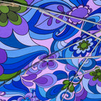 Close-up of a patterned umbrella canopy with a retro psychedelic design in shades of blue, purple, and green, with white metal ribs crossing diagonally.