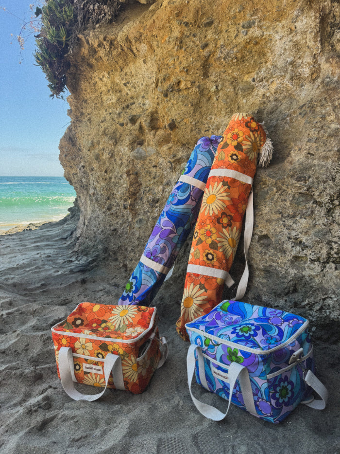 umbrellas in their bags leaned up against a rock wall by the beach with matching coolers