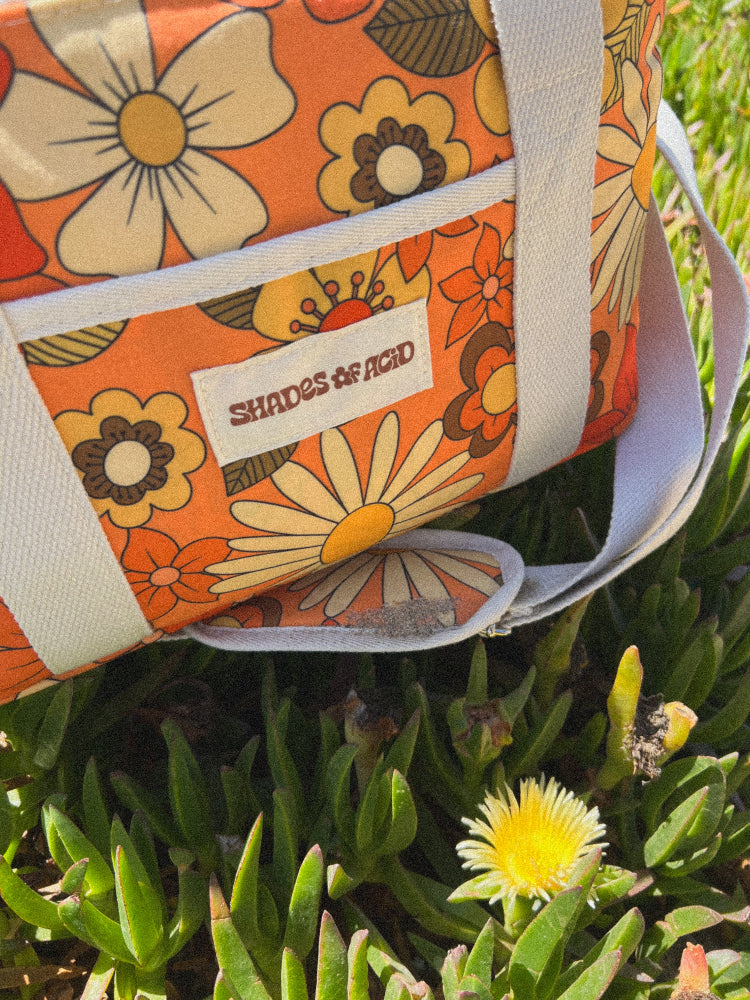 close up photo of retro floral ice cooler bag sitting on ice plant by a yellow flower