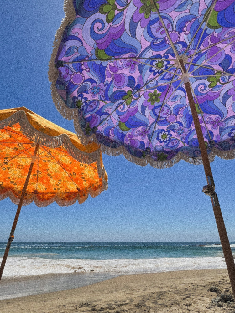 photo of an orange floral and purple floral  beach umbrellas with tan fringe in the sand with the ocean in the background